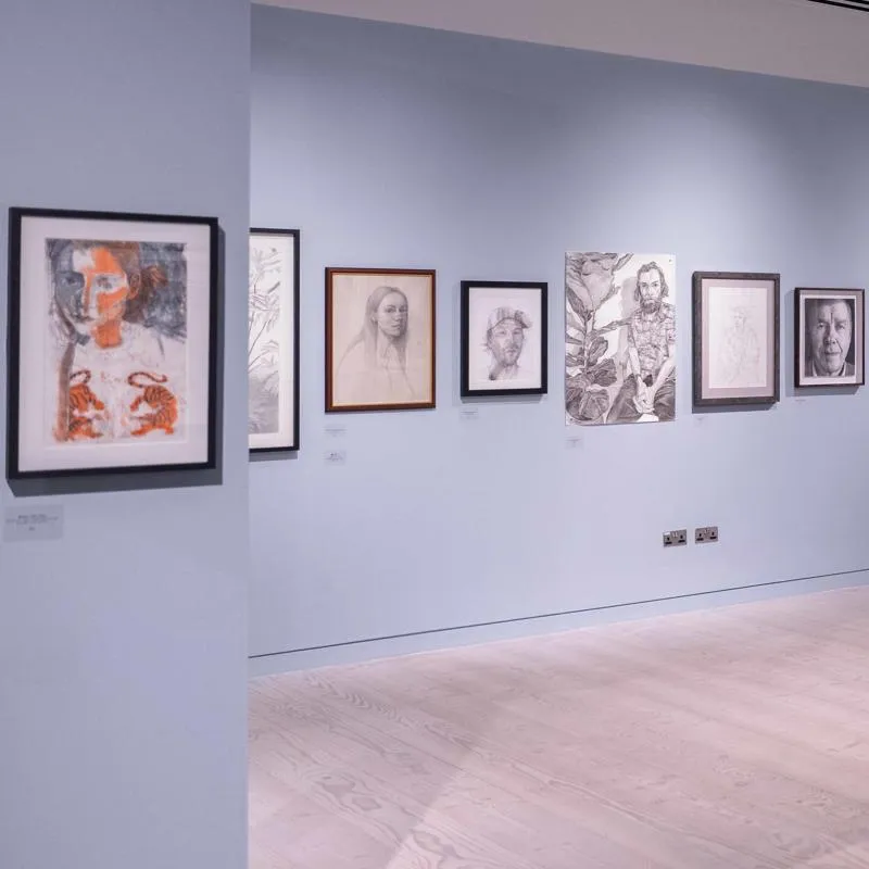 A spacious art gallery with blue walls displays lots of framed sketches and portraits.