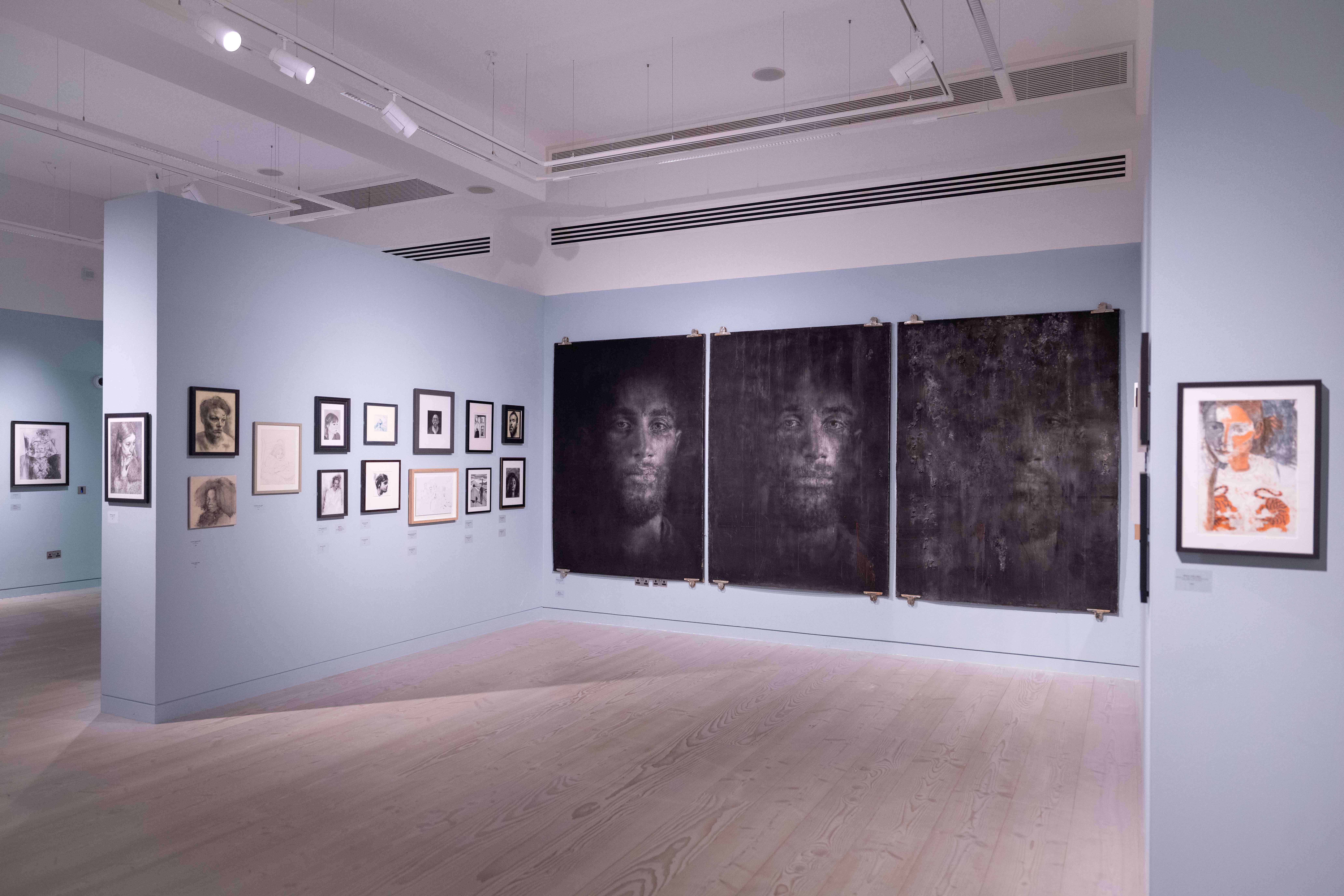 Art gallery with light blue walls displaying black-and-white portraits and sketches.
