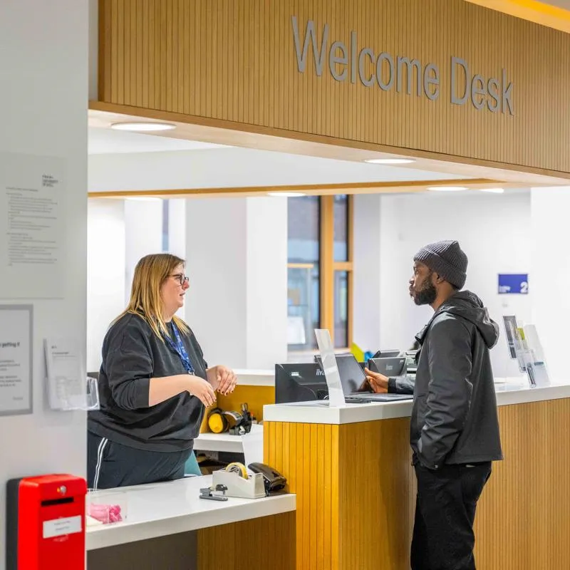 Visitor at the reception desk speaking to a member of the Library Staff